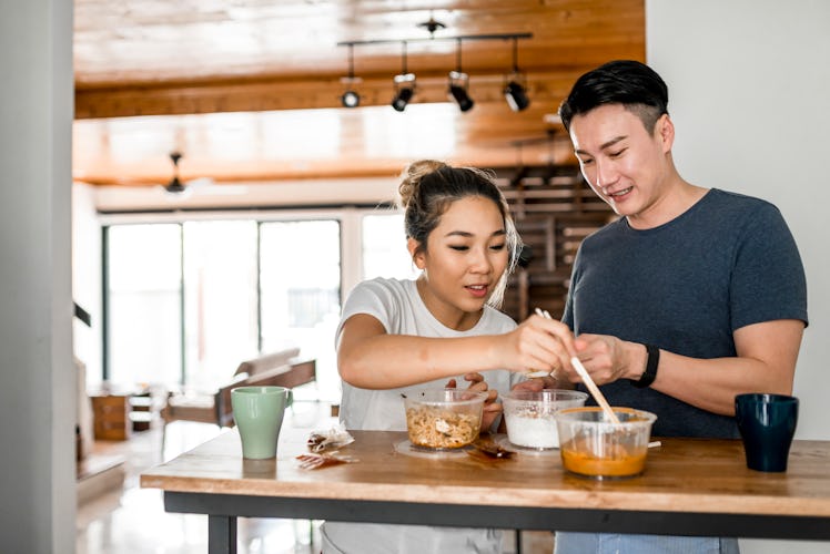 A couple sits at the counter in their kitchen and splits containers of food.