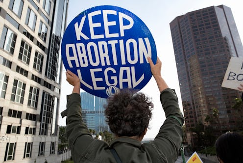 People standing in a crowd holding signs reading, "Keep Abortion Legal." Virginia lawmakers just rem...