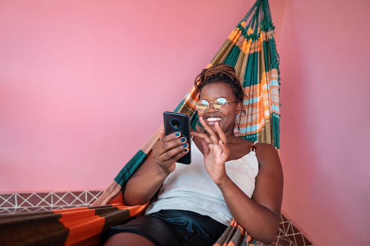 A young woman relaxes in a hammock surrounded by a pink wall while writing a belated birthday messag...