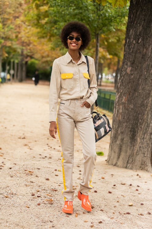 A woman with an afro hair wearing a beige athleisure suit with yellow details and orange sneakers