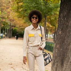 A woman with an afro hair wearing a beige athleisure suit with yellow details and orange sneakers