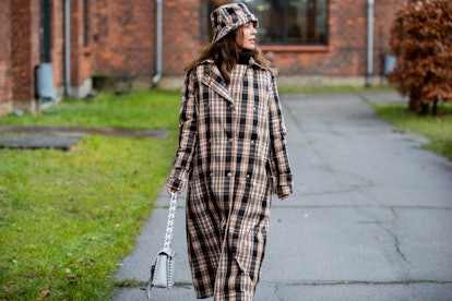 A brunette woman walking in a black-beige plaid coat and bucket hat, and a white purse at the Copenh...