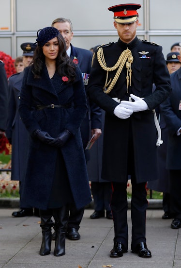 Meghan Markle and Prince Harry at a funeral, with Harry's hands above his torso as if protecting it 