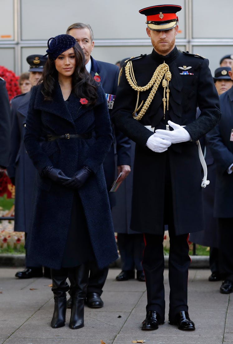 Meghan Markle and Prince Harry at a funeral, with Harry's hands above his torso as if protecting it 