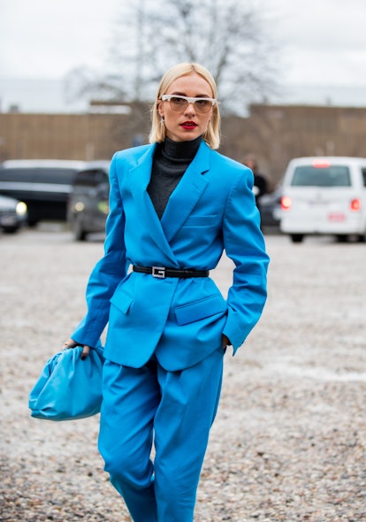 A blonde woman in a blue suit, black turtleneck, black belt and a blue purse at the Copenhagen Fashi...