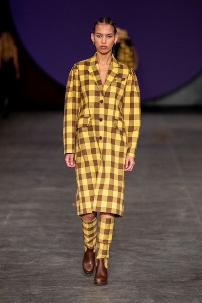 Model wears a yellow-and-brown checkered raincoat-come-dress with matching boots by Baum und Pferdga...