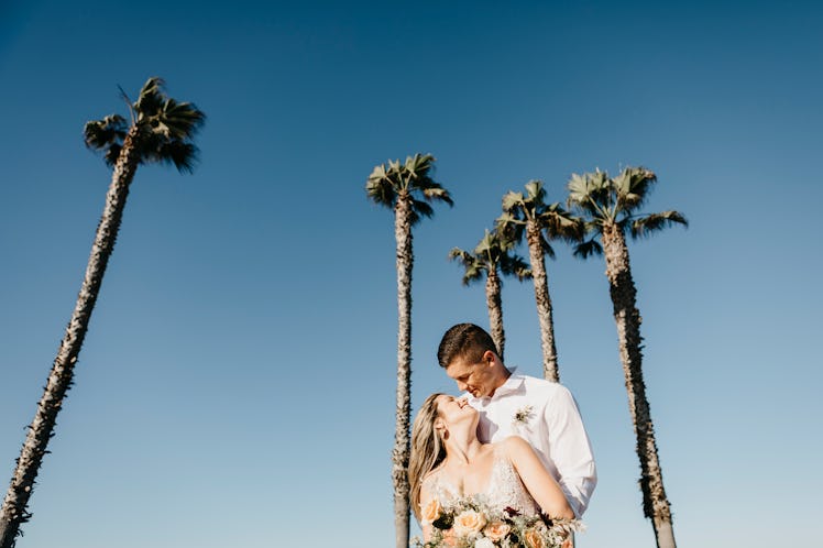 A couple stands under palm trees while eloping in California.