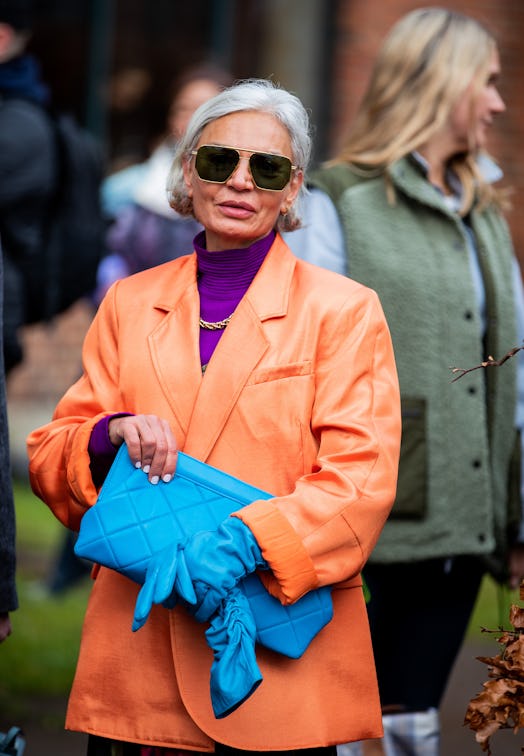 A woman in an orange blazer, purple turtleneck, blue gloves and purse at the Copenhagen Fashion Week