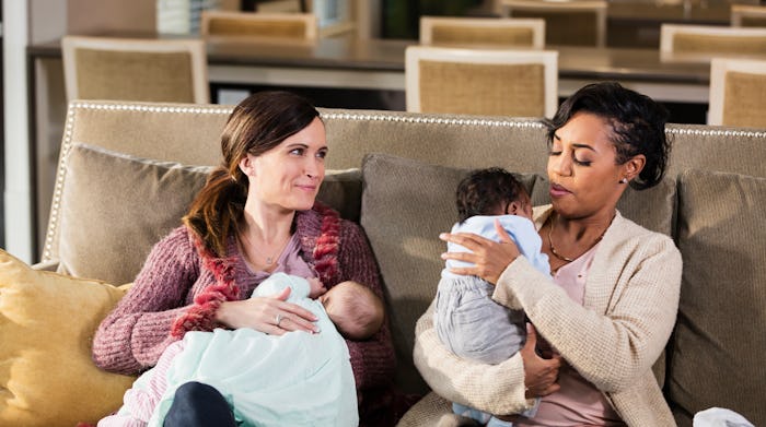 two moms on couch, one breastfeeding