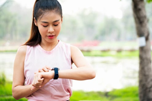 A person wearing a pink mesh tank top checks her smart watch during an outdoor workout. You don't ne...