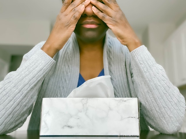 A woman covers her eyes, leaning on a tissue box. Stress has a number of impacts on the body, research shows