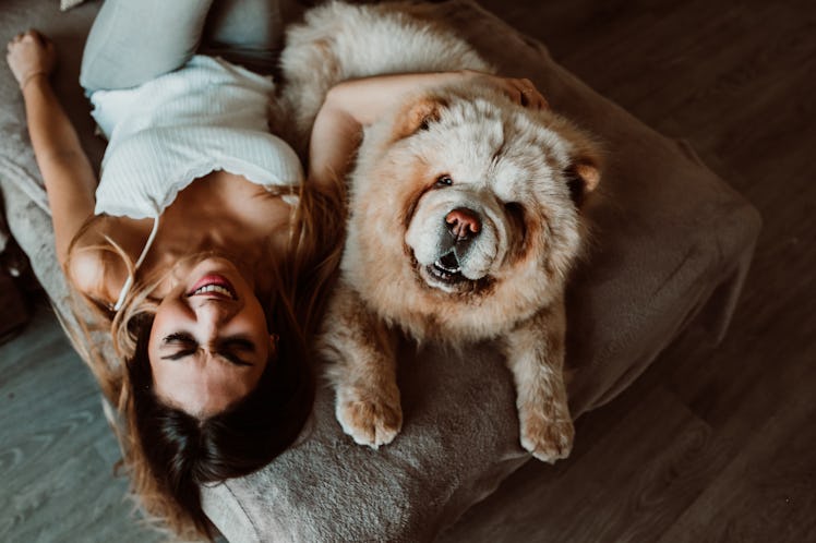 A woman lays on her bed with her very fluffy dog in the middle of the afternoon.