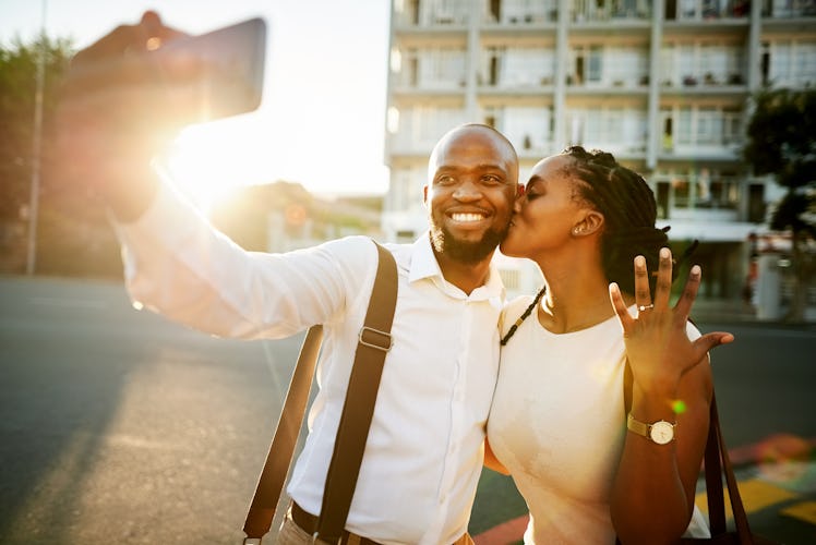 A young couple take a picture on their phone at sunset after getting engaged.