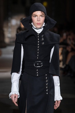A female model walking in a black cloak jacket at a fashion show