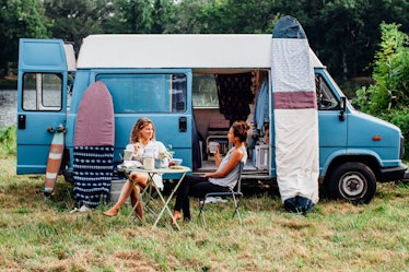 Two friends sit outside of their campervan in the middle of spring and eat breakfast. 