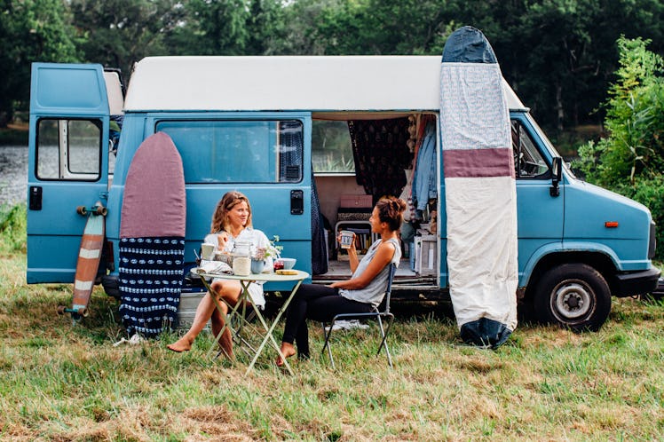 Two friends sit outside of their campervan in the middle of spring and eat breakfast.