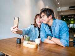 A cute couple takes a funny selfie while sitting at a table in a restaurant.