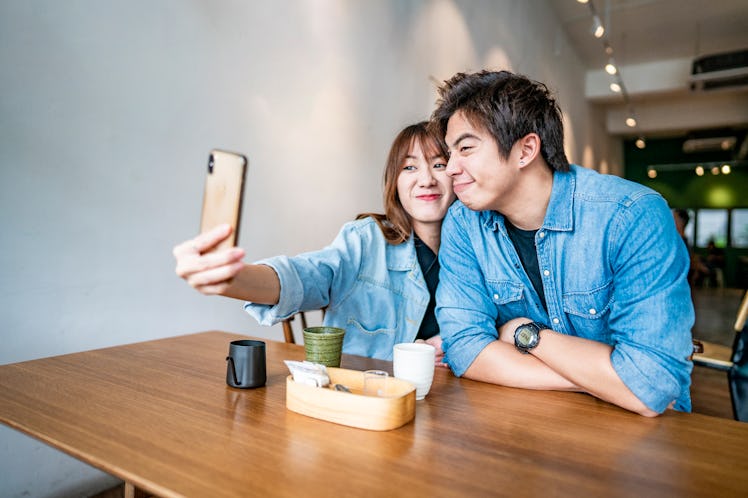 A cute couple takes a funny selfie while sitting at a table in a restaurant.