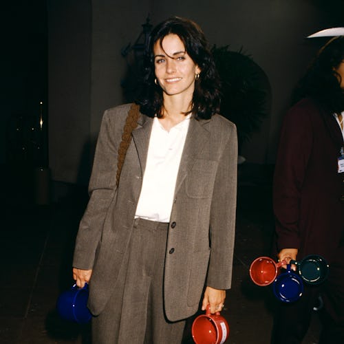 Courteney Cox wearing a khaki suit and a white t-shirt, smiling for a photo.