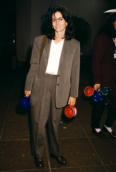 Courteney Cox wearing a khaki suit and a white t-shirt, smiling for a photo.