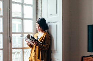 A young woman reads a magazine in the window of her apartment.