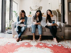 Three girls sit on a couch and play the best iPhone games on their phones.