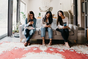 Three girls sit on a couch and play the best iPhone games on their phones.