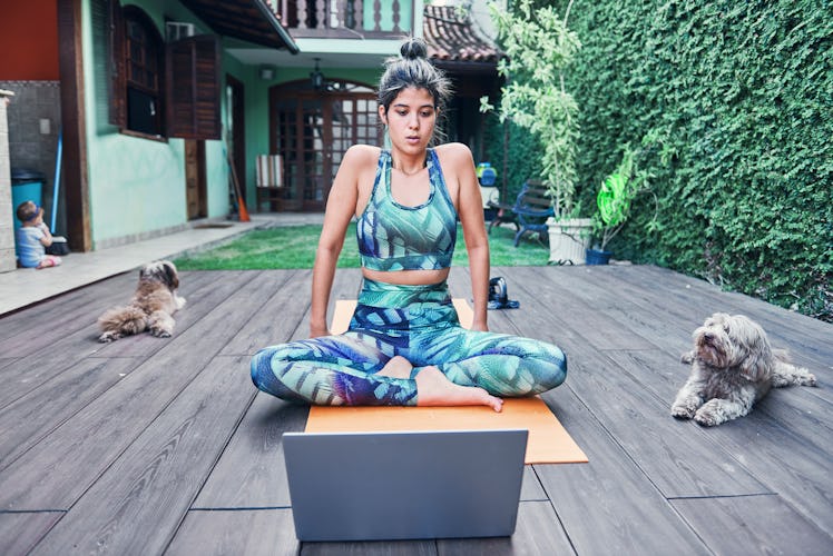 A young woman follows a yoga with your dog video tutorial while sitting on her back porch with her p...
