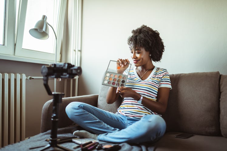 A young woman poses with a set of watercolors while having a photo shoot at home.