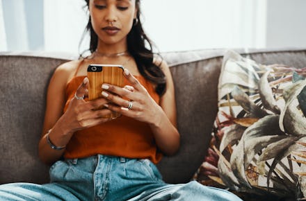A woman with Coronavirus anxiety sitting on a couch and typing on her phone