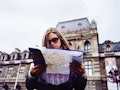 A young woman stands outside the Louvre in Paris with a map.