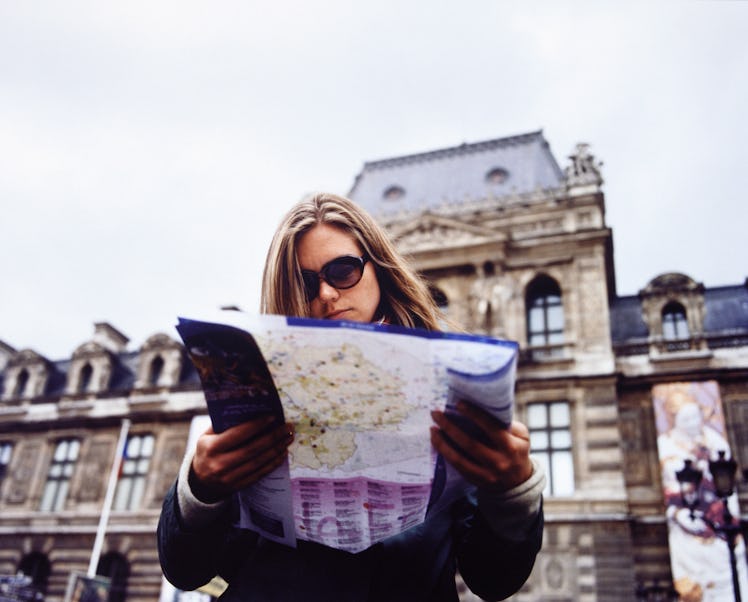 A young woman stands outside the Louvre in Paris with a map.