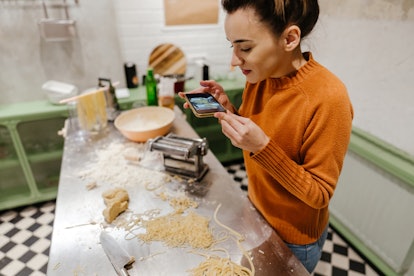 A young woman takes a picture on her phone of the homemade pasta she just made.