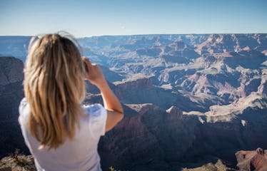 A blonde woman takes a picture of the Grand Canyon while visiting the national park.