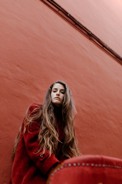 A fashionable woman poses against a red wall in a red jacket.