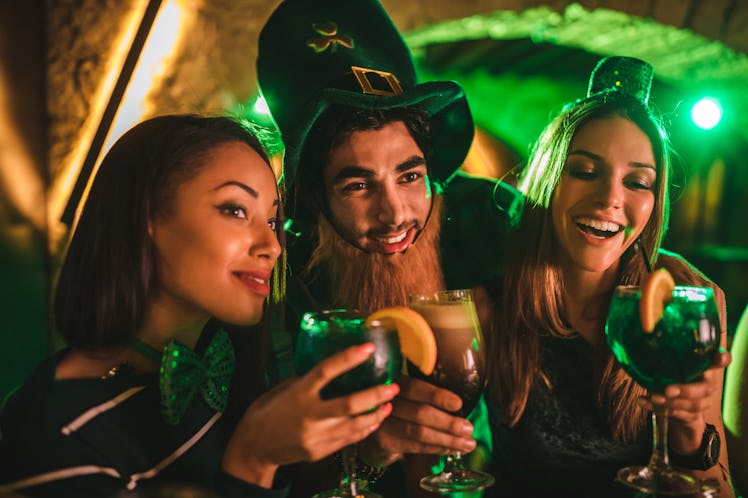 Three friends toast their drinks at a bar on St. Patrick's Day.