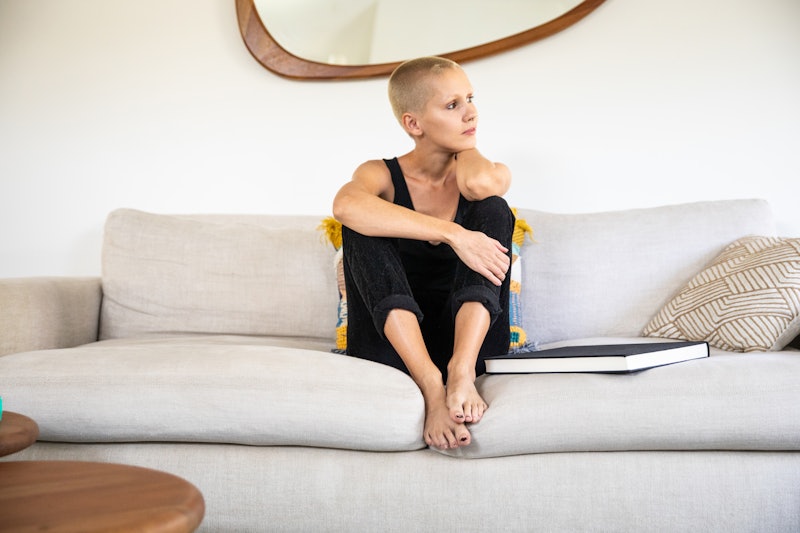 A woman with a shaved head sits on her couch at home. If you need to calm down quickly, these expert...