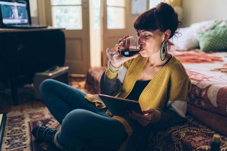 A woman sips her wine while on a virtual call in her home.