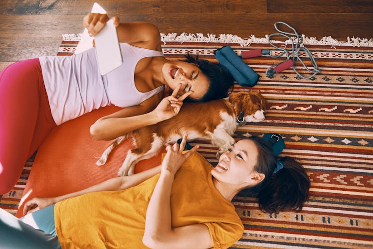 Two friends lay on the floor with their dog while video chatting their friends.