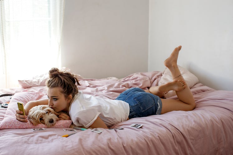 A young woman lays on her bed with her dog while on FaceTime with her SO.