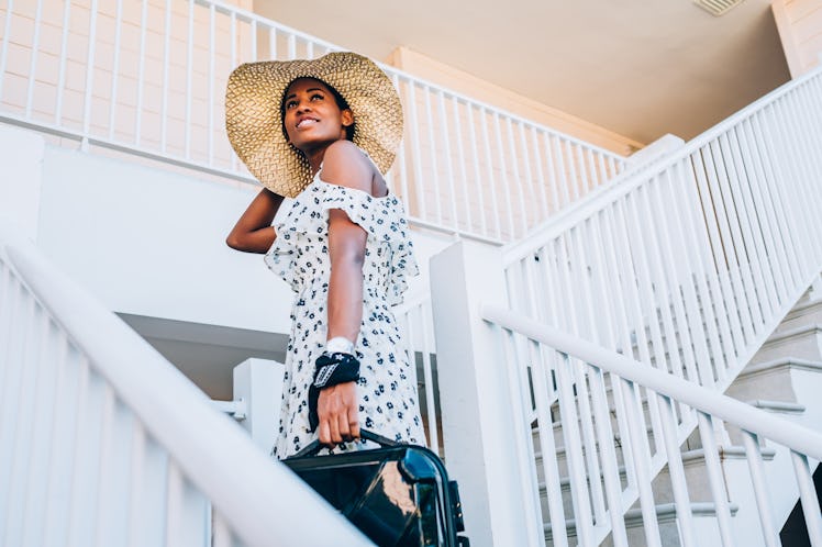 A young woman walks up a flight of stairs a hotel with a suitcase in her hand.