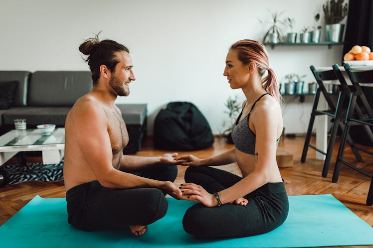 A young couple does yoga in their apartment on a bright blue mat.
