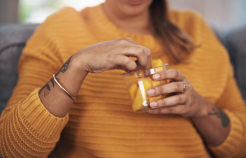 A woman in a yellow sweater eats mangos out of a jar. Women With OCD Share How They’re Coping During...