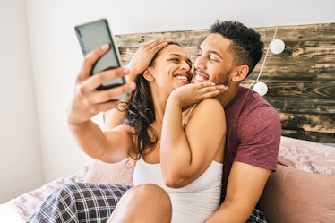 A couple laughs while using Instagram story filters on their phone and hanging out in bed.