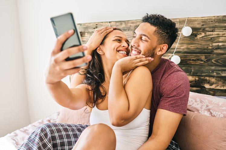 A couple laughs while using Instagram story filters on their phone and hanging out in bed.