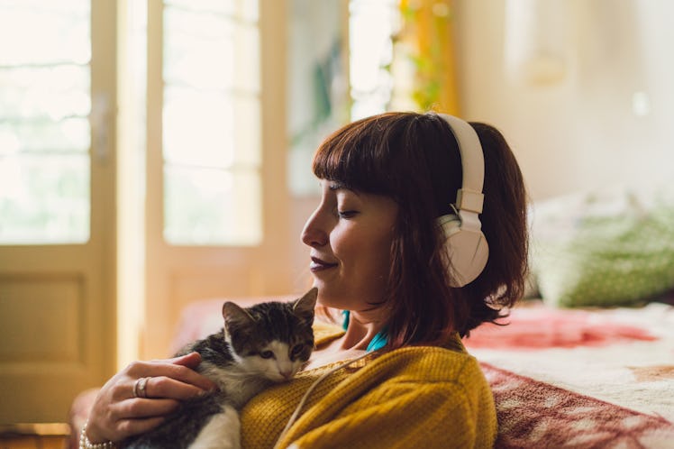 A woman sits in her bedroom and listens to guided meditation while holding her kitten.