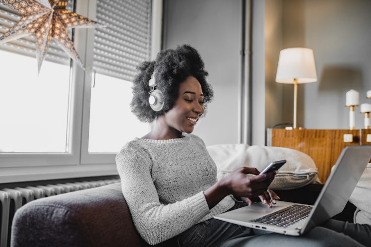 A woman sits with her phone and laptop while working from home.