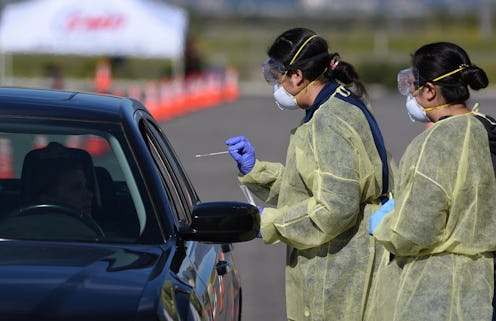 Two workers in PPE administer COVID-19 tests in a drive through testing facility.