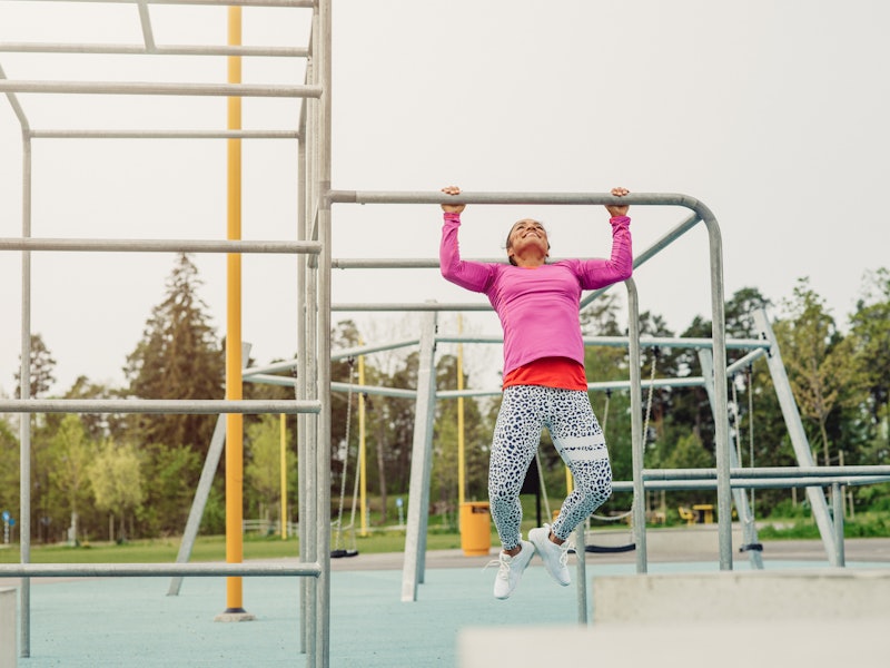 A person smiles as she does pullups in a jungle gym. High-energy workouts can help reduce your anxie...