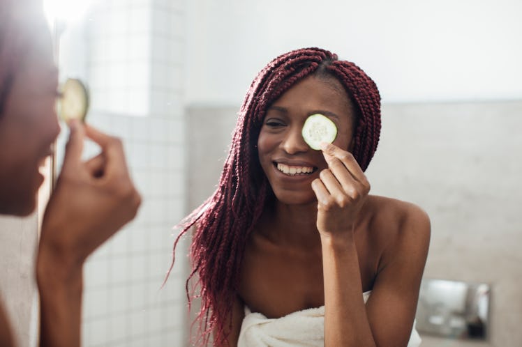 A young woman poses in the mirror at a spa, while wearing a bath towel and holding a cucumber slice ...